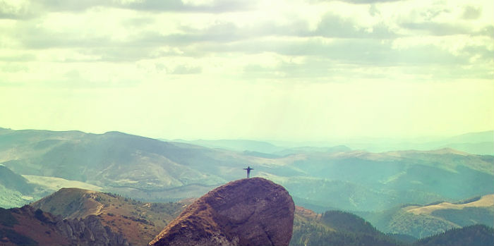 person spreading her arms to the sky at the top of a mountain, seen from very far