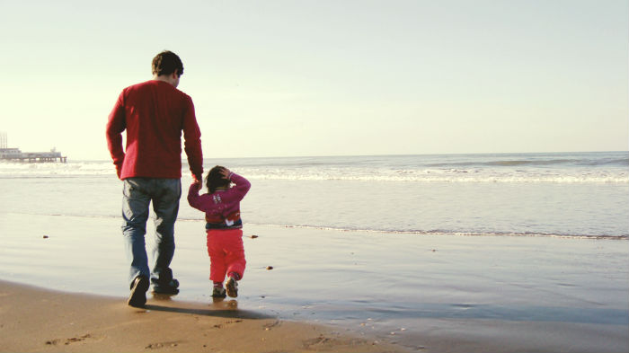 father and small child daughter waling in beach holding hands