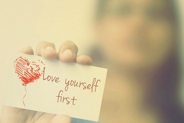 woman holding paper card saying love yourself first